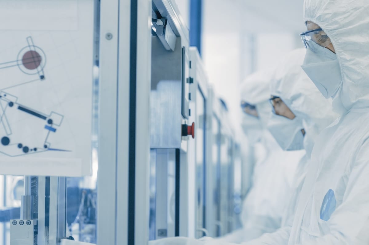 In the Manufacturing Facility Team of Scientist Wearing Sterile Protective Coverall Set’s up / Programs Modern Industrial 3D Printer, High Precision Manufacture of Semiconductors under Process.